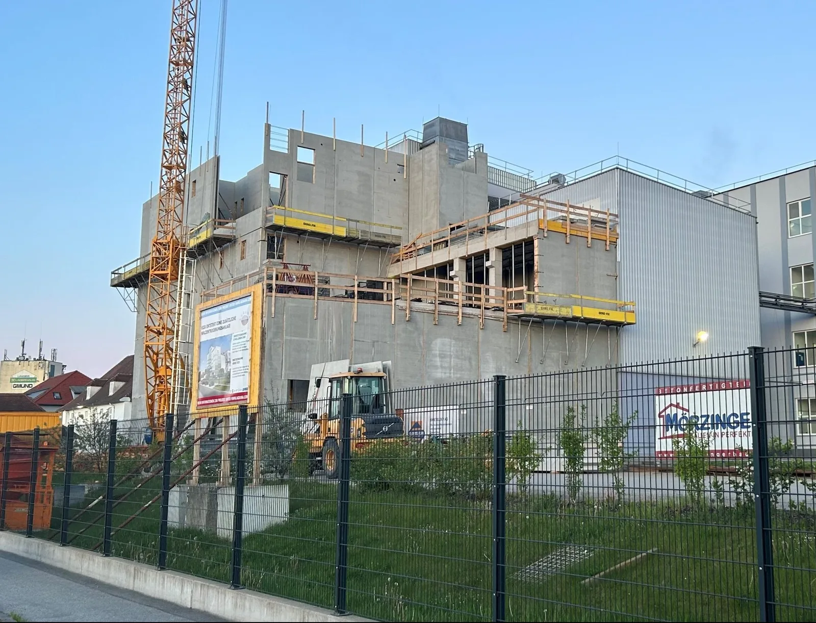 Mehrgeschossiger Rohbau mit Turmkran, am Bauzaun eine Mörzinger-Werbetafel