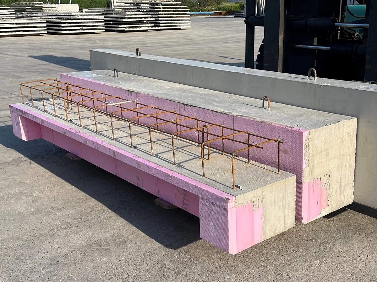 Fertigteilträger mit rosa Dämmung und herausragender Bewehrung auf dem Werksgelände