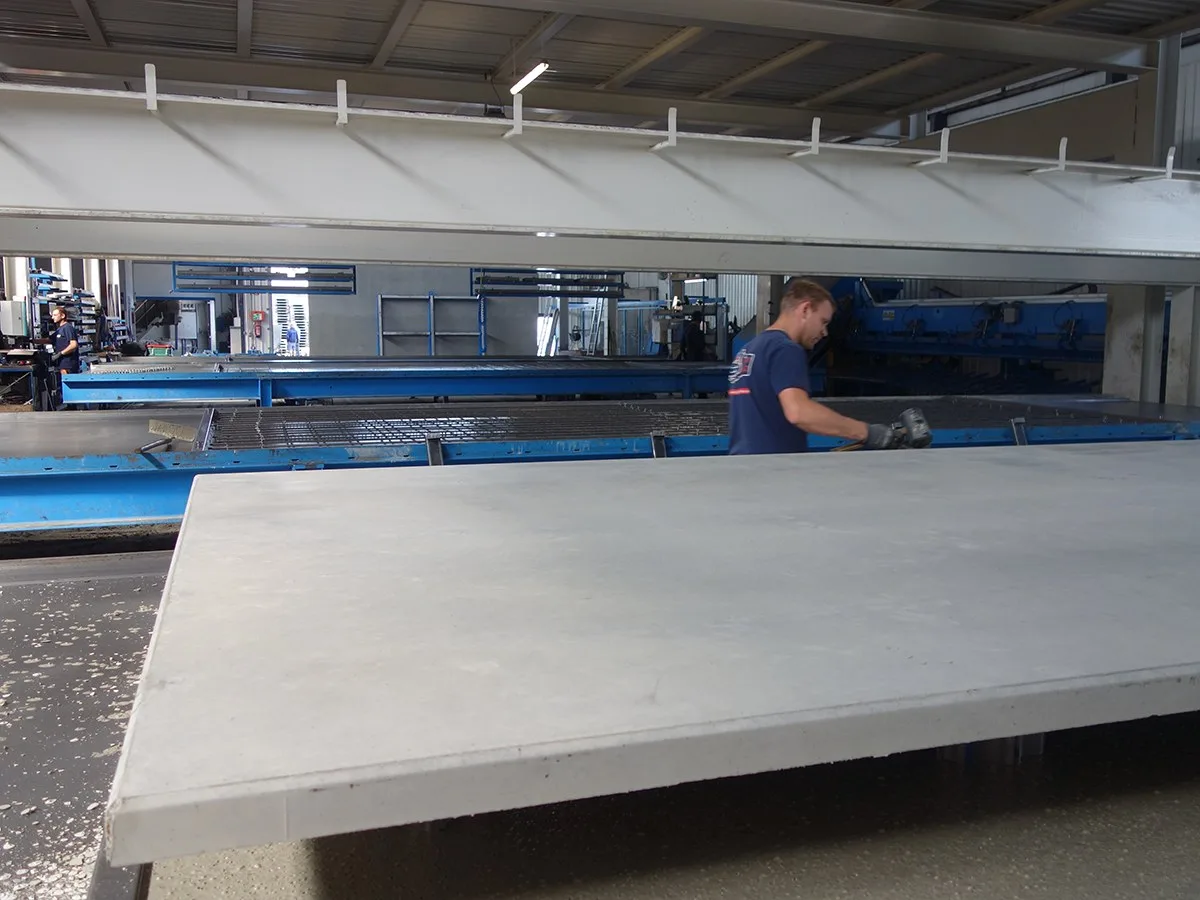 Produktionshalle mit großen Schalungstischen, ein Mitarbeiter arbeitet am fertigen Element